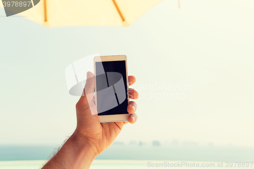 Image of close up of male hand holding smartphone on beach