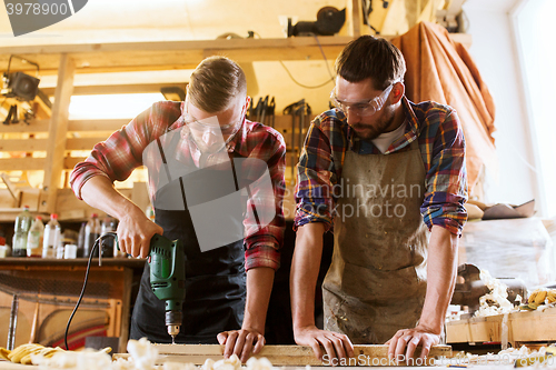 Image of carpenters with drill drilling plank at workshop