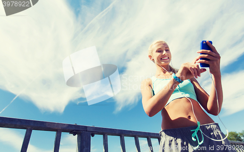 Image of happy woman with smartphone and earphones outdoors