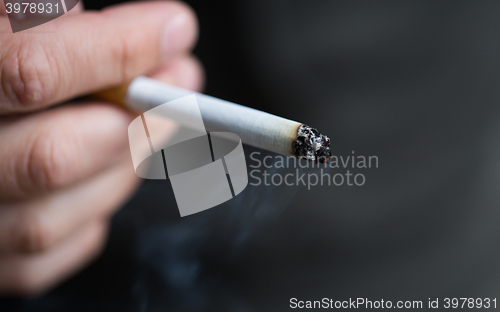 Image of close up of male hand with smoking cigarette