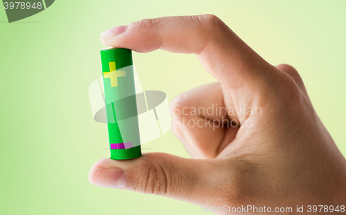 Image of close up of hand holding green alkaline battery