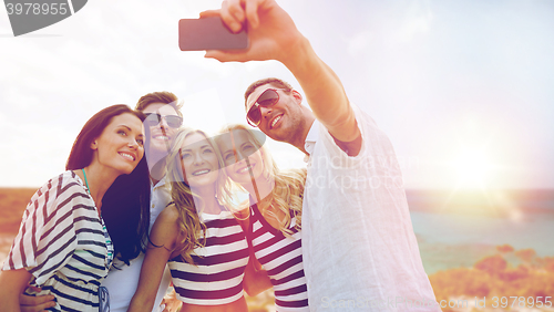Image of happy friends taking selfie by smartphone on beach