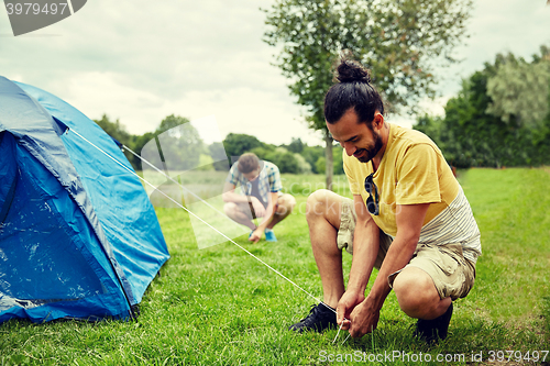 Image of smiling friends setting up tent outdoors