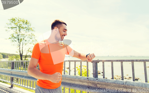 Image of smiling young man with smart wristwatch at seaside