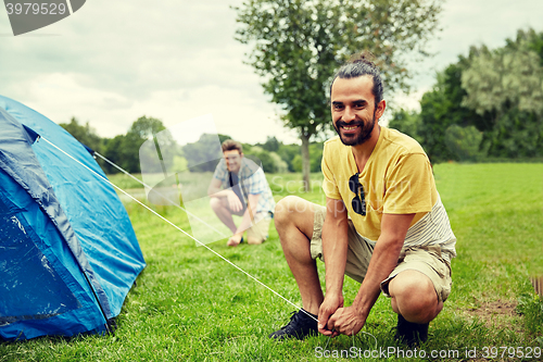 Image of smiling friends setting up tent outdoors
