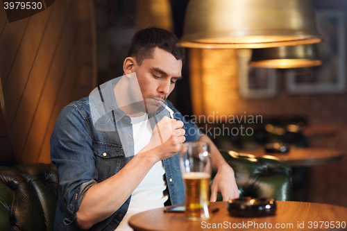 Image of man drinking beer and smoking cigarette at bar