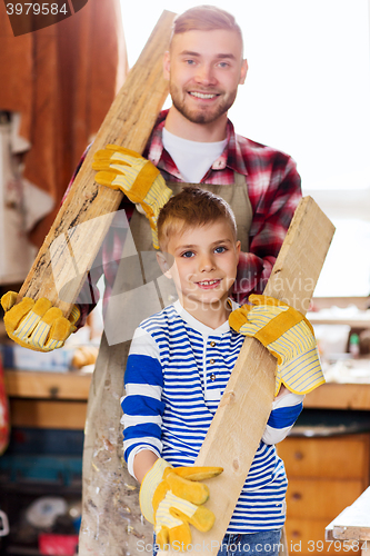 Image of happy father and son with wood plank at workshop