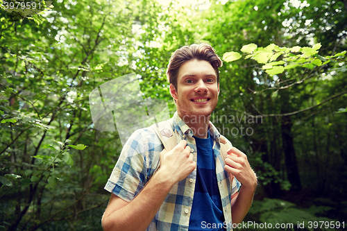 Image of smiling young man with backpack hiking in woods