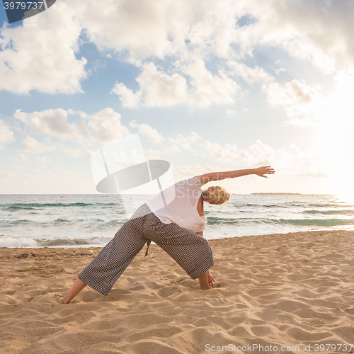 Image of Woman practicing yoga on sea beach at sunset.