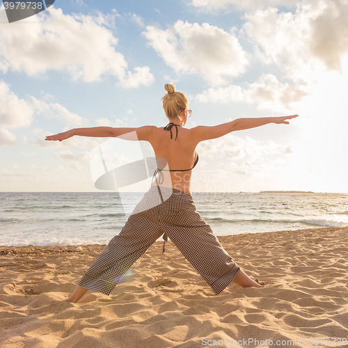 Image of Woman practicing yoga on sea beach at sunset.