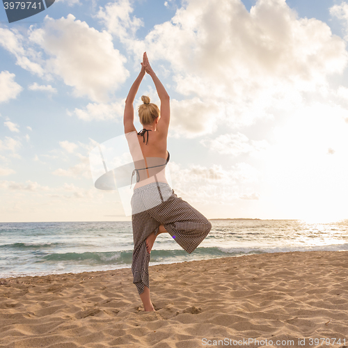 Image of Woman practicing yoga on sea beach at sunset.