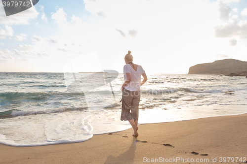 Image of Woman walking on sand beach at golden hour