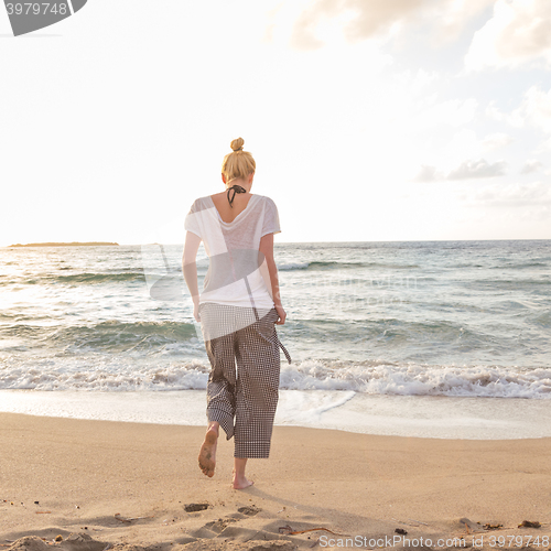 Image of Woman walking on sand beach at golden hour