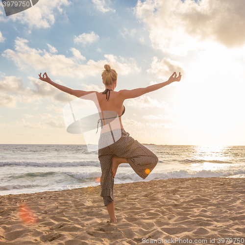 Image of Woman practicing yoga on sea beach at sunset.
