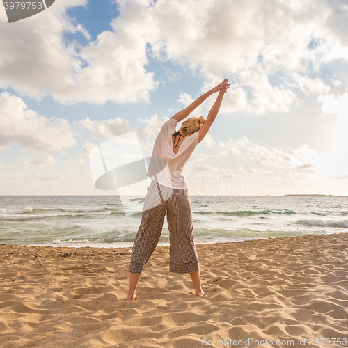 Image of Woman practicing yoga on sea beach at sunset.