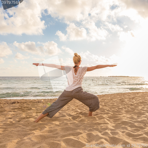 Image of Woman practicing yoga on sea beach at sunset.