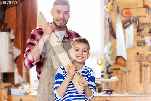 Image of happy father and son with wood plank at workshop