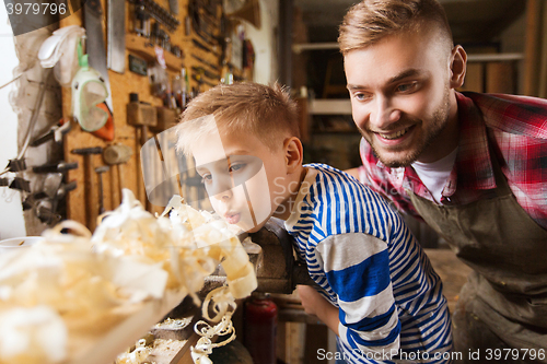 Image of father and little son with wood plank at workshop