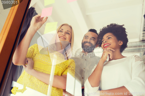 Image of happy creative team writing on stickers at office