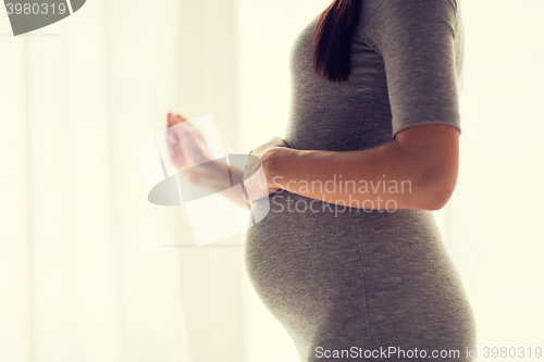 Image of pregnant woman looking through window at home