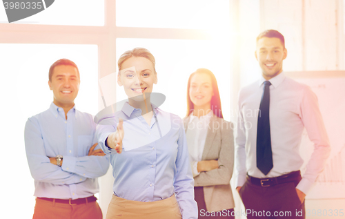 Image of smiling businesswoman in office with team on back