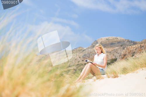 Image of Woman reading book, enjoying sun on beach.