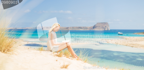 Image of Woman reading book, enjoying sun on beach.