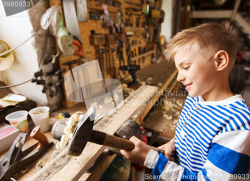 Image of happy little boy with hammer and plank at workshop