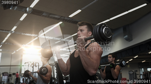 Image of group of men flexing muscles with barbell in gym