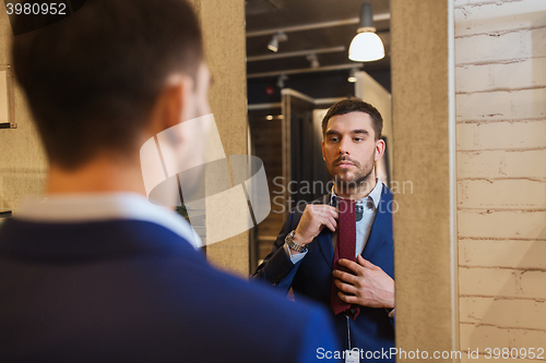 Image of man trying tie on at mirror in clothing store