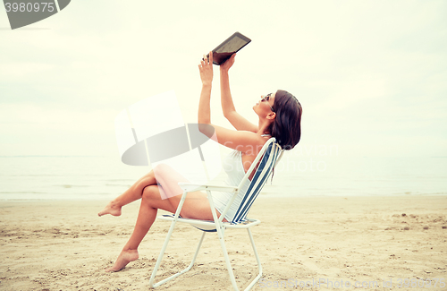 Image of happy woman with tablet pc taking selfie on beach