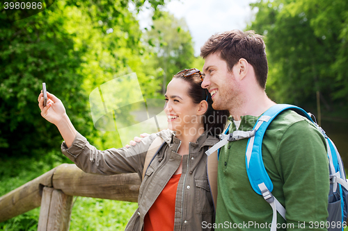 Image of couple with backpacks taking selfie by smartphone