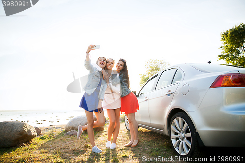 Image of happy women taking selfie near car at seaside