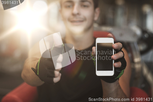 Image of young man with smartphone showing thumbs up in gym