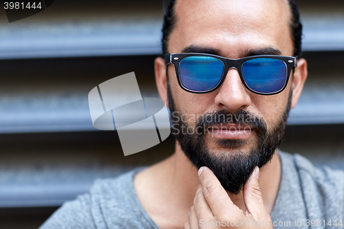 Image of man in sunglasses touching beard on city street