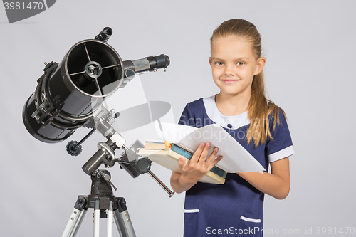 Image of Schoolgirl astronomer leafing through books standing at the telescope