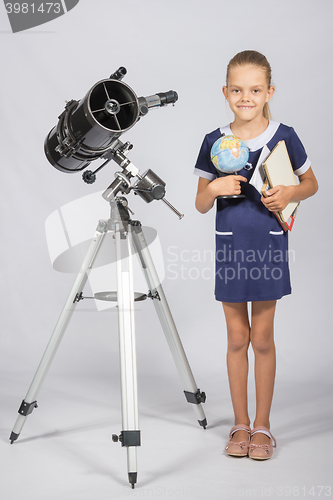 Image of Schoolgirl astronomer is a telescope with a globe and books in the hands