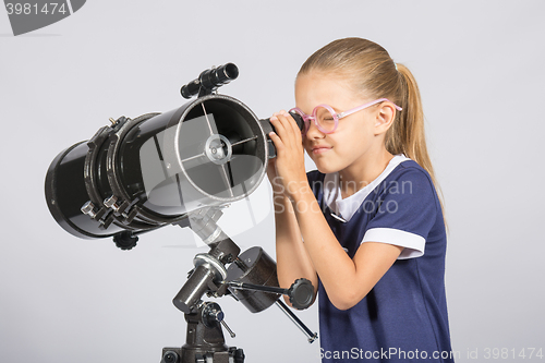 Image of Seven-year girl in glasses with interest looks in a reflector telescope