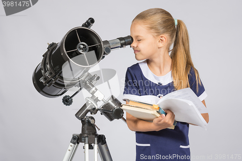 Image of School girl looking through a telescope standing with textbooks