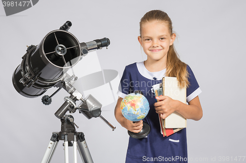 Image of Girl astronomer is a telescope with a globe and books in the hands