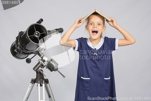 Image of Schoolgirl covered her head with a textbook and cry looking at the frame, standing at the telescope