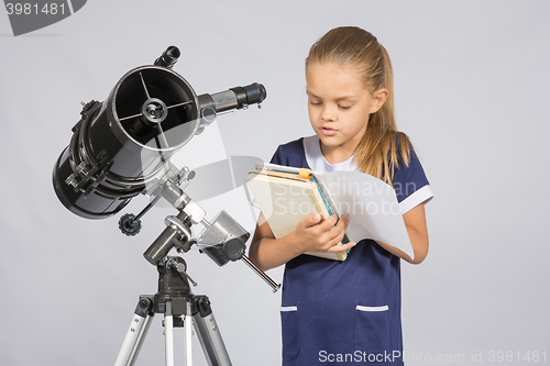 Image of Schoolgirl reading a textbook while standing astronomer at the telescope