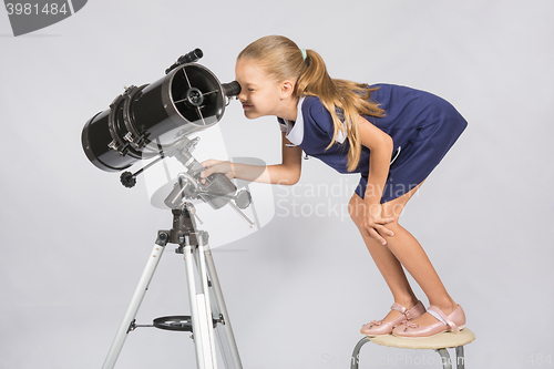 Image of Seven-year girl standing on a chair and looks ridiculous in the eyepiece of the telescope reflector