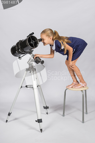 Image of The young astronomer standing on a chair and funny looking in a telescope eyepiece