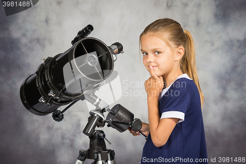 Image of Seven-year girl thoughtfully looks in the picture, standing at the telescope