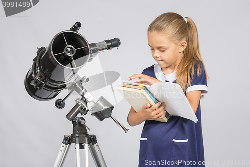 Image of Schoolgirl astronomer leafing through books to find the right information at the stand of the telescope