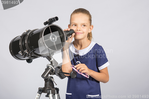 Image of Seven-year girl standing next to a reflector telescope and looks mysteriously into the sky