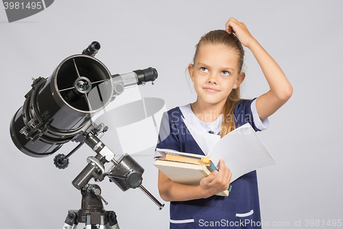 Image of Schoolgirl wondered and looked up to by reading a textbook while standing at the telescope