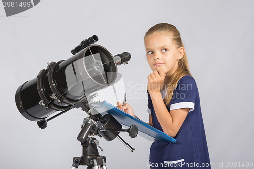 Image of Seven-year girl thoughtful looking at the sky, making the recording of observations in the telescope