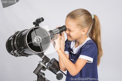 Image of Seven-year girl squinting with interest looks in a reflector telescope